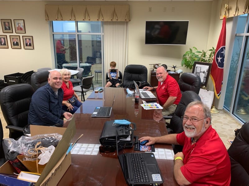 A group of people are sitting around a table with laptops.