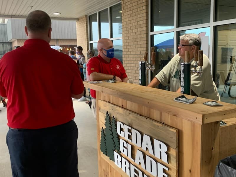 A man in a red shirt is standing in front of a cedar glade brewing bar.