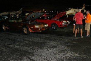 A group of people are looking at cars in a parking lot at night