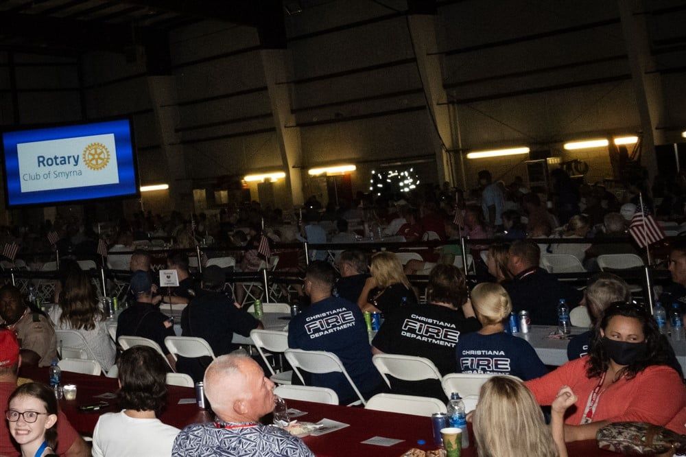 A group of people are sitting at tables in front of a screen that says rotary on it.