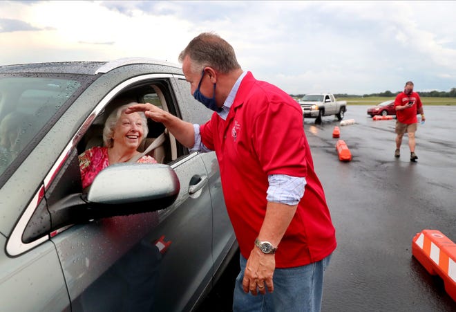 A man in a red shirt is talking to an older woman in a car.