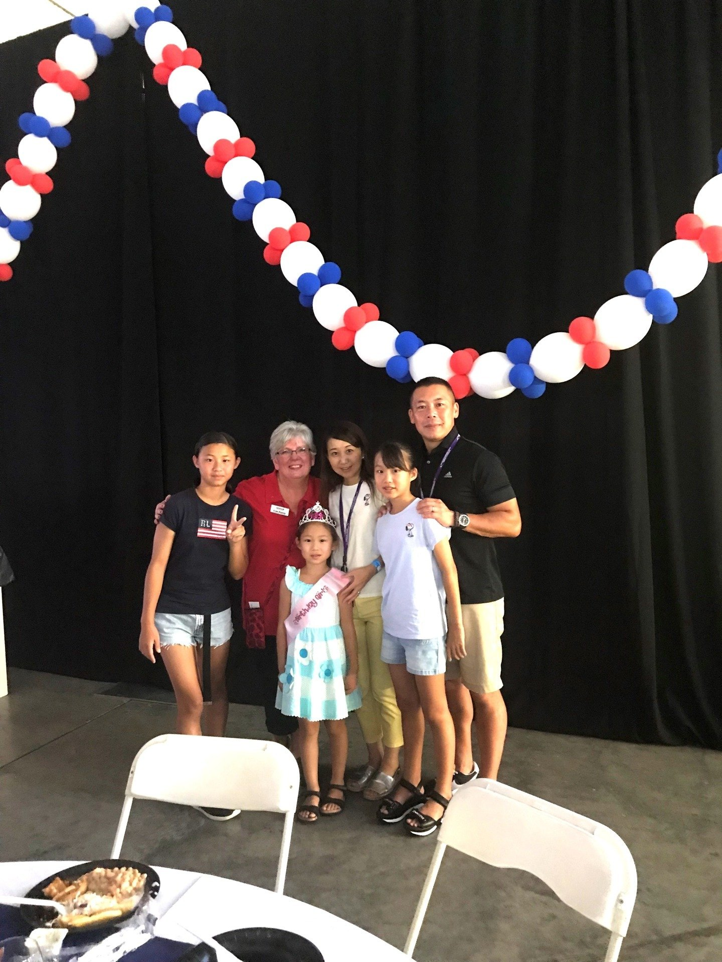 A group of people standing around a table with balloons hanging from the ceiling.