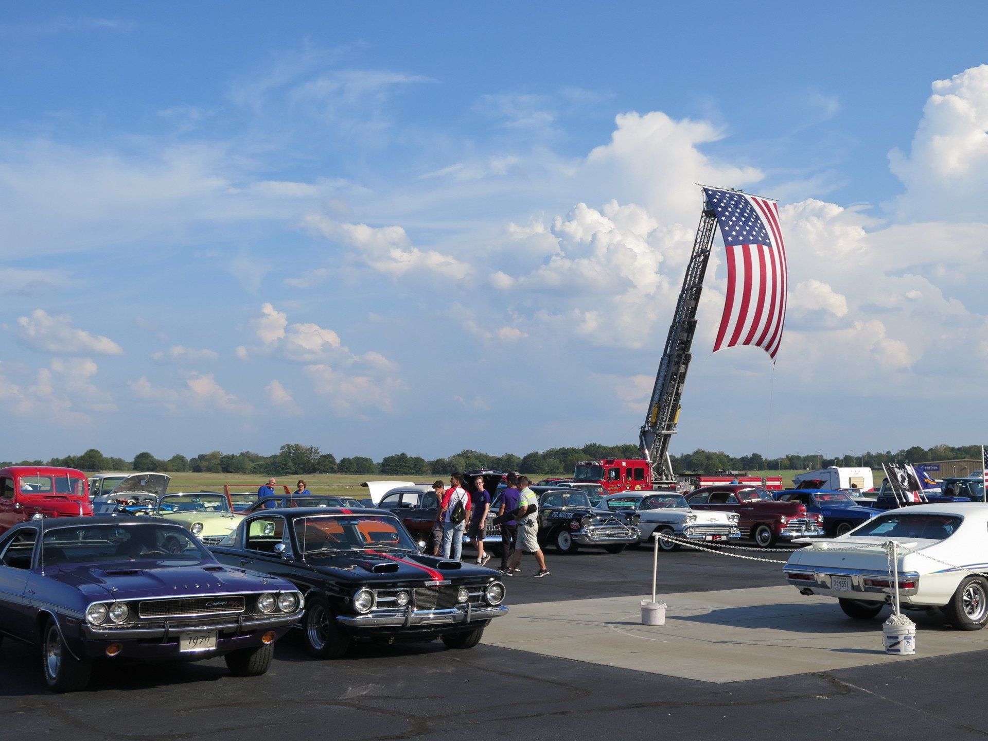 A group of cars are parked in a parking lot with an american flag flying in the background