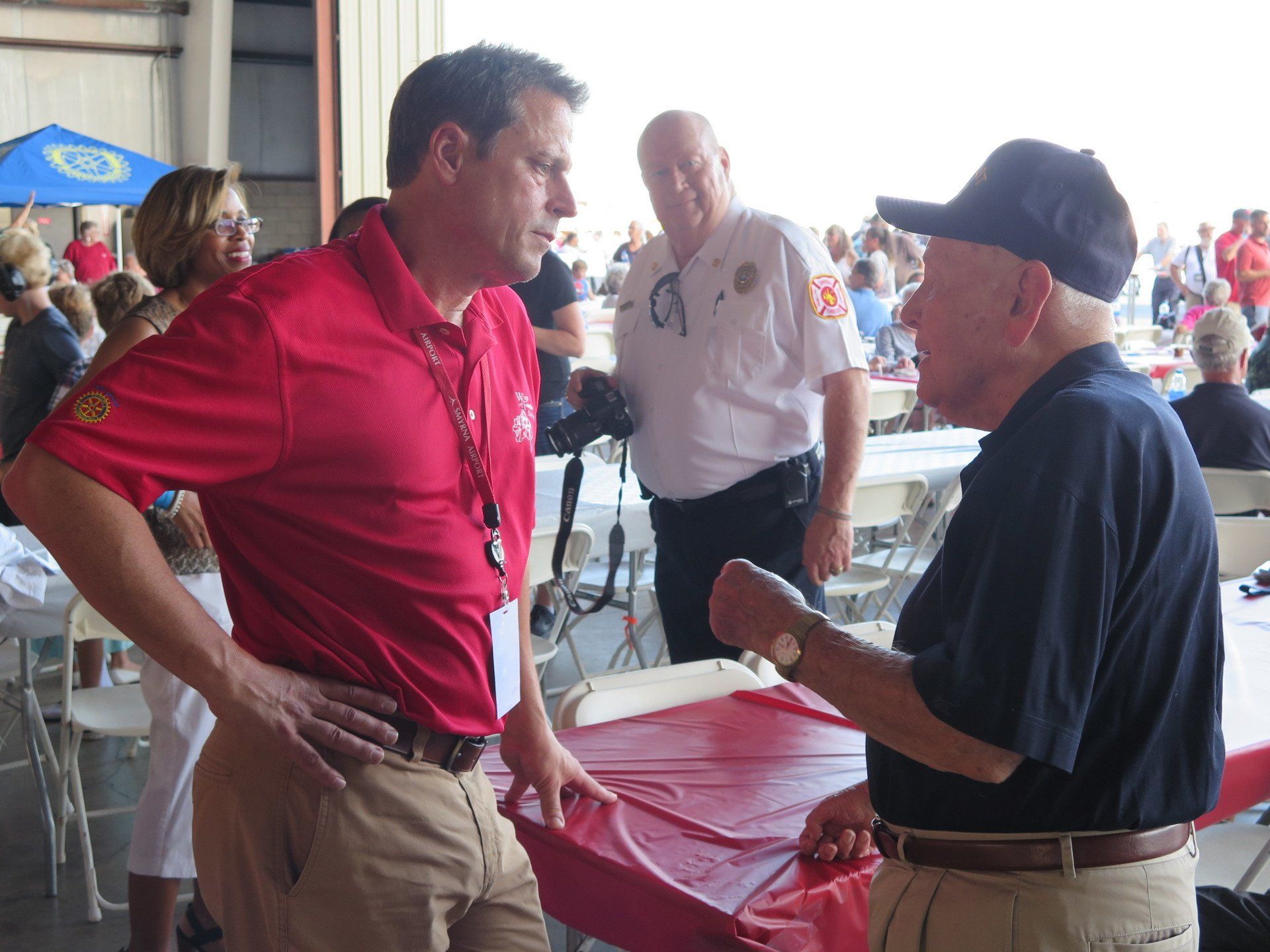 A man in a red shirt is talking to another man