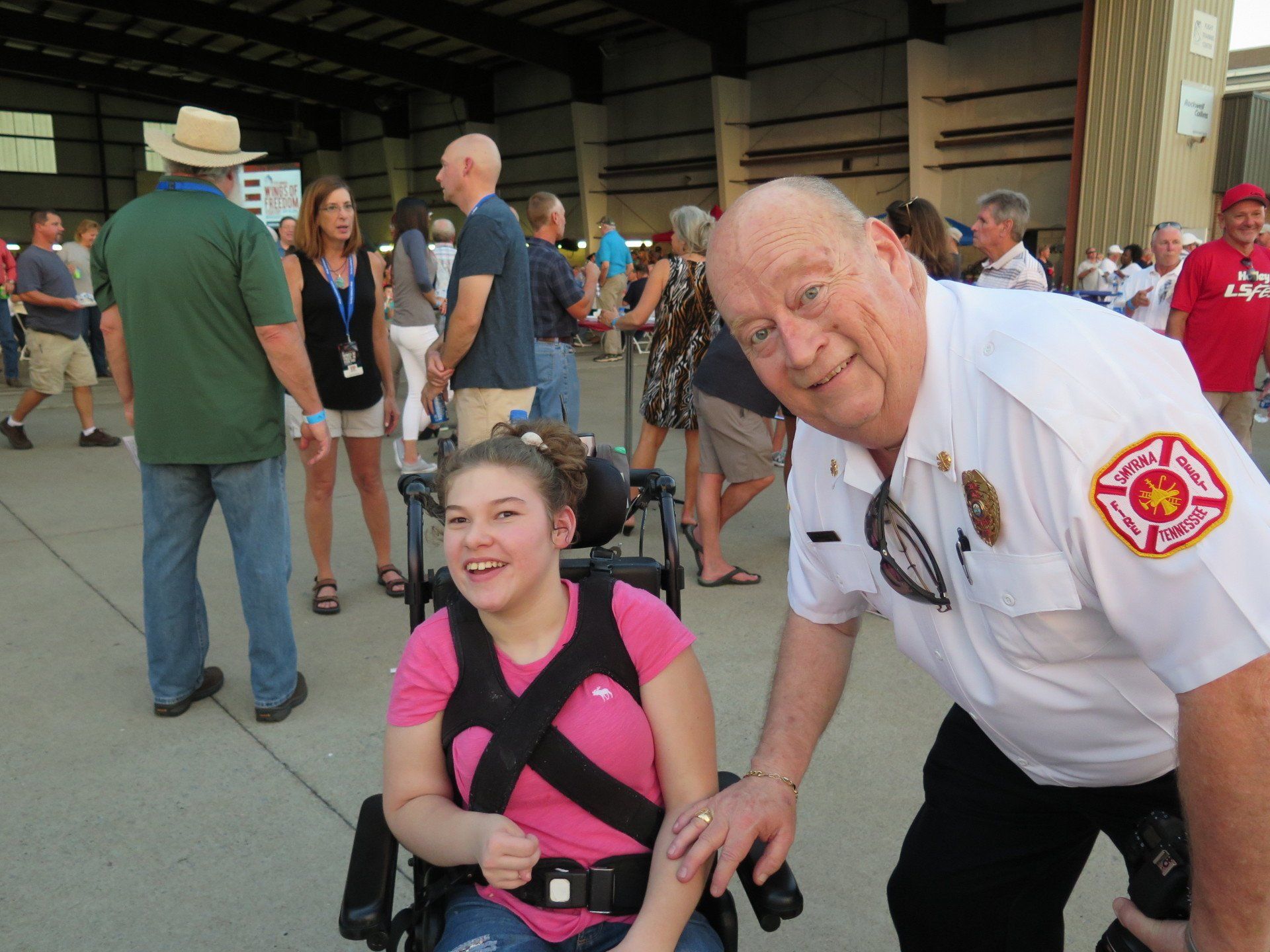 A man in a firefighter uniform stands next to a girl in a wheelchair