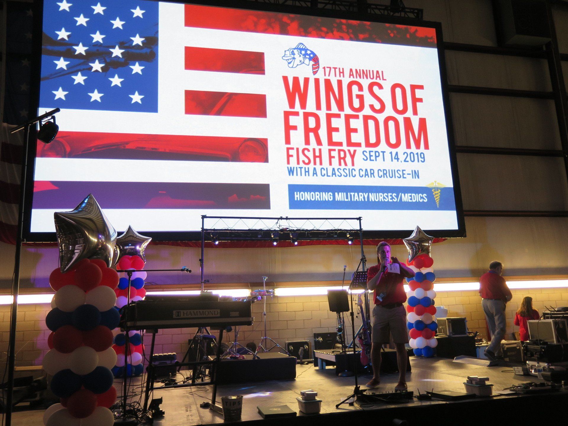 A man stands on a stage in front of a large screen that says wings of freedom
