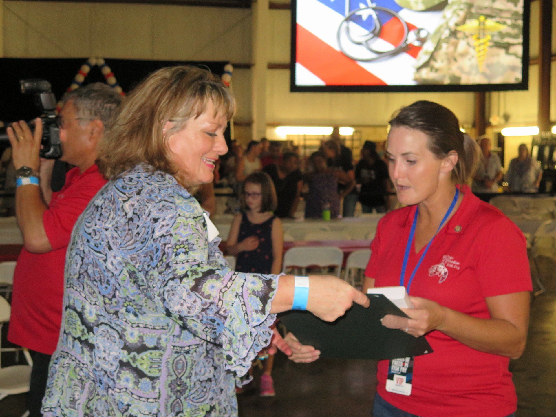 A woman in a red shirt is shaking hands with another woman
