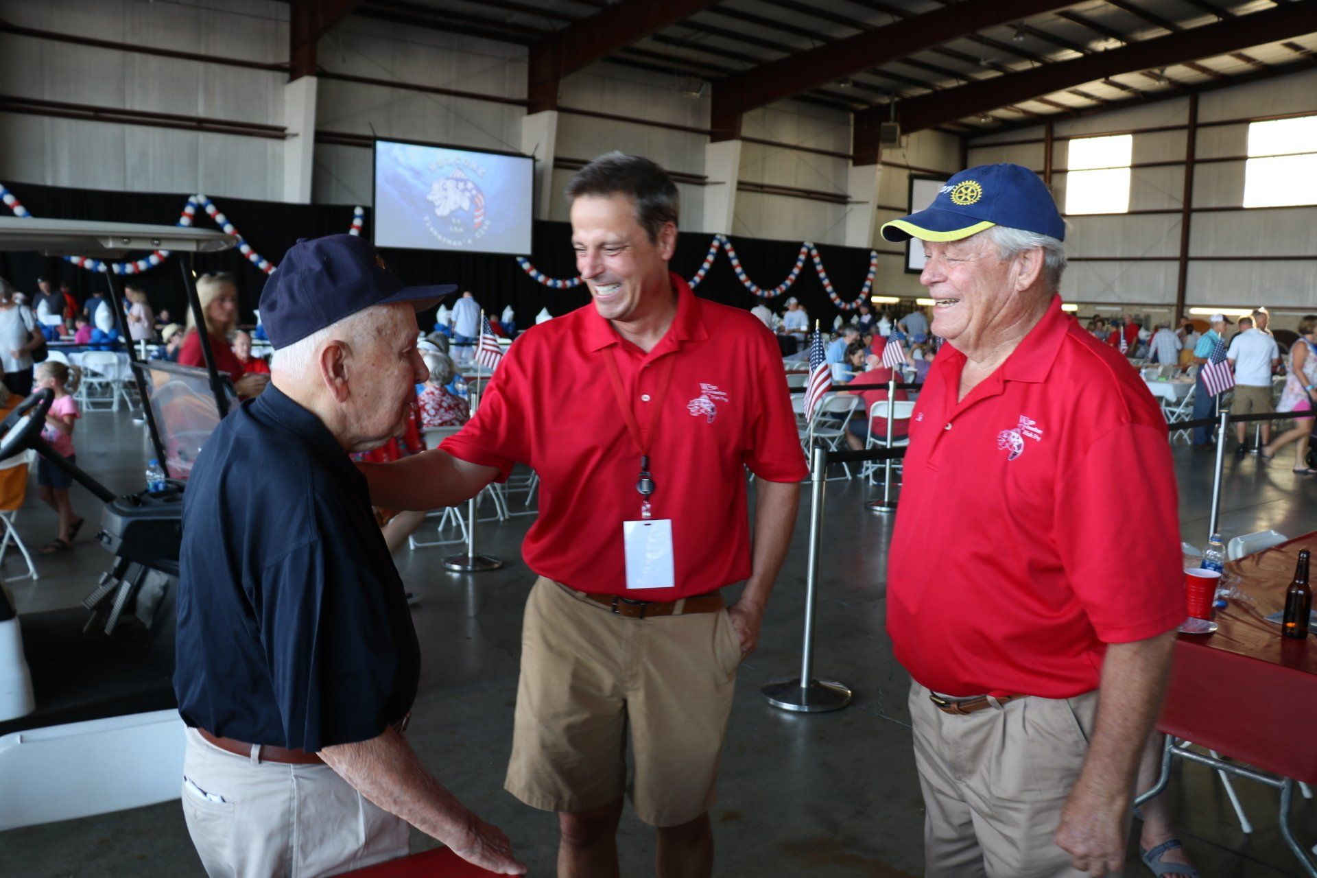 Three men in red shirts are standing in a room talking to each other.