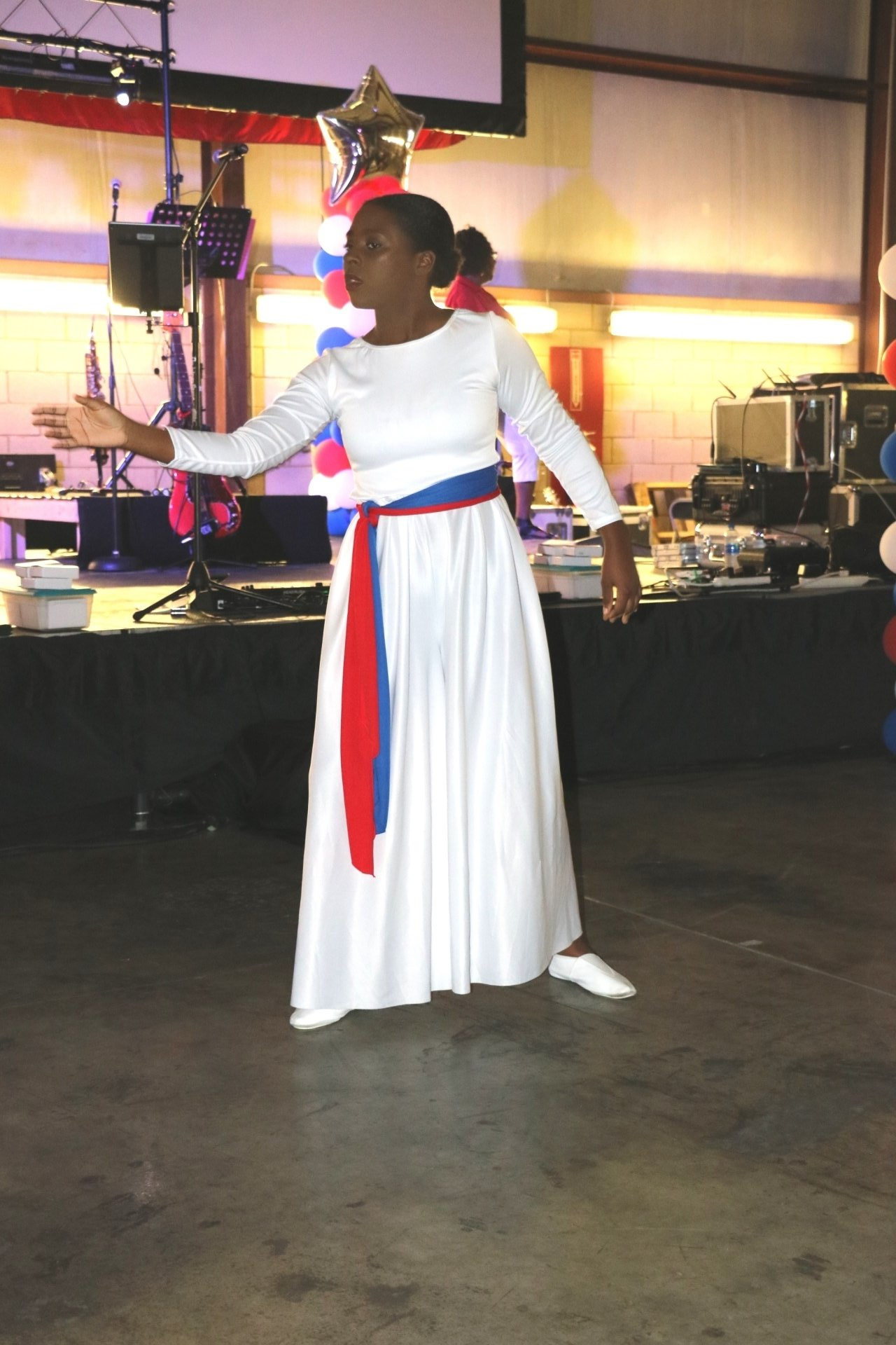 A woman in a white dress with a red and blue sash around her waist