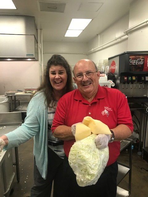 A man and a woman are posing for a picture in a kitchen with a coca cola machine in the background