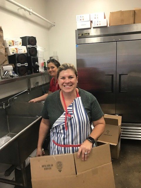 A woman in an apron is holding a cardboard box in a kitchen