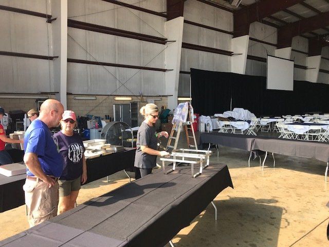 A group of people are standing around tables in a large room.