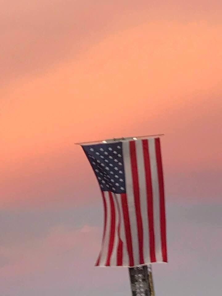 An american flag is hanging from a pole with a sunset in the background