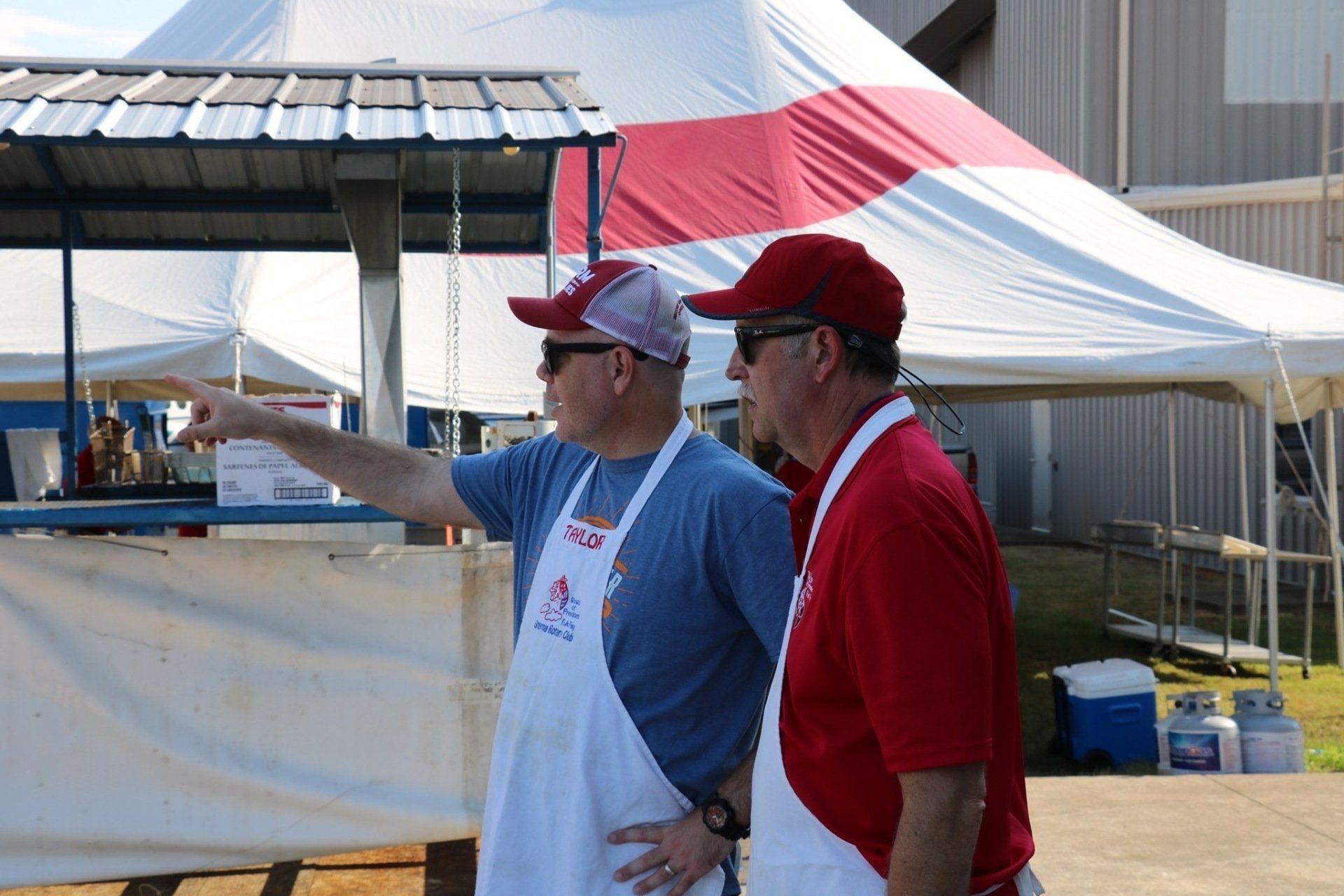 Two men wearing aprons are standing in front of a tent.