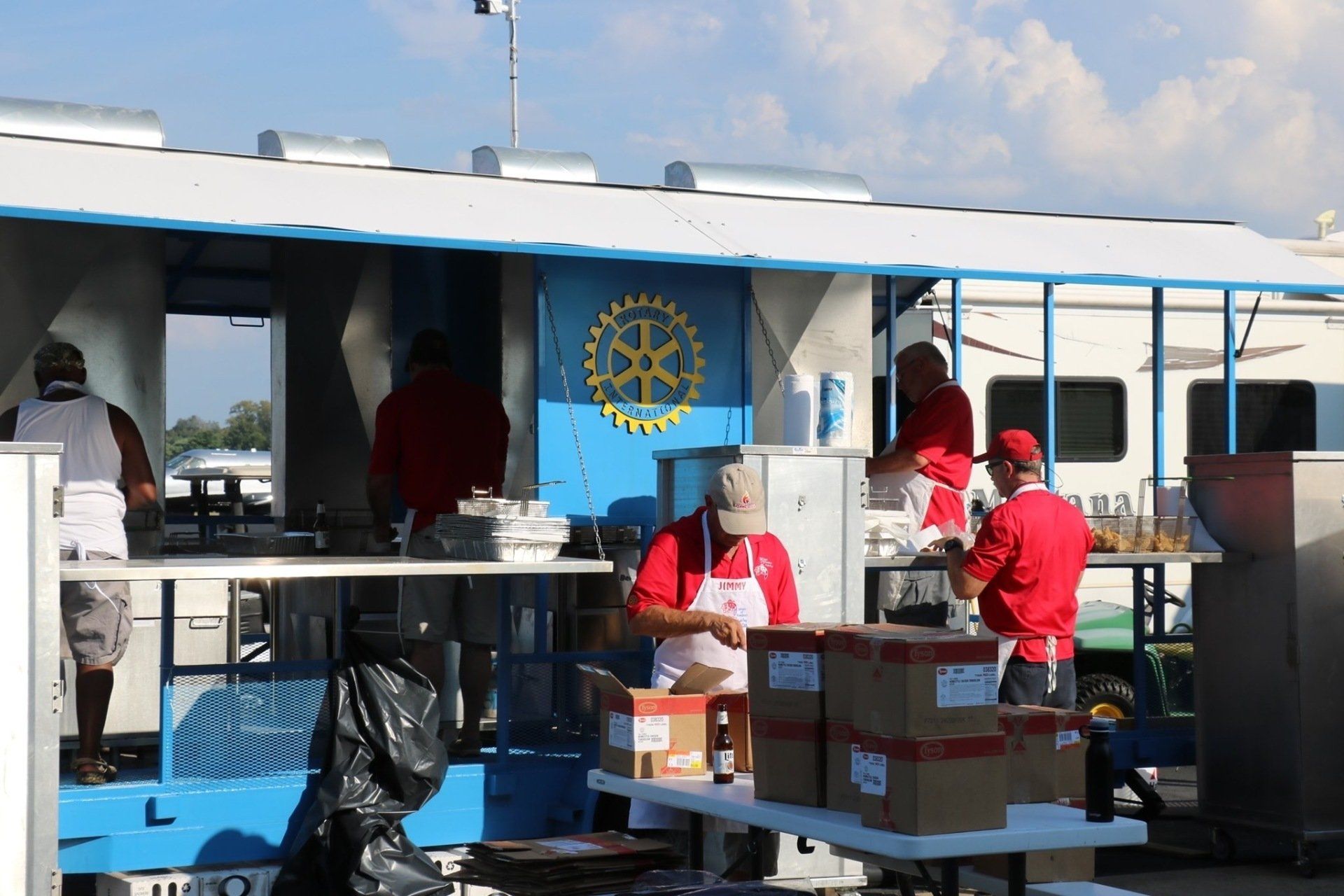 A group of people are preparing food in front of a building with a rotary logo on it