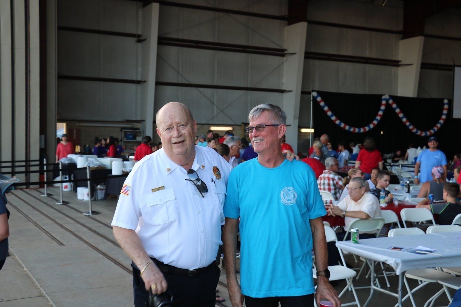 A man in a blue shirt is standing next to a man in a white uniform.