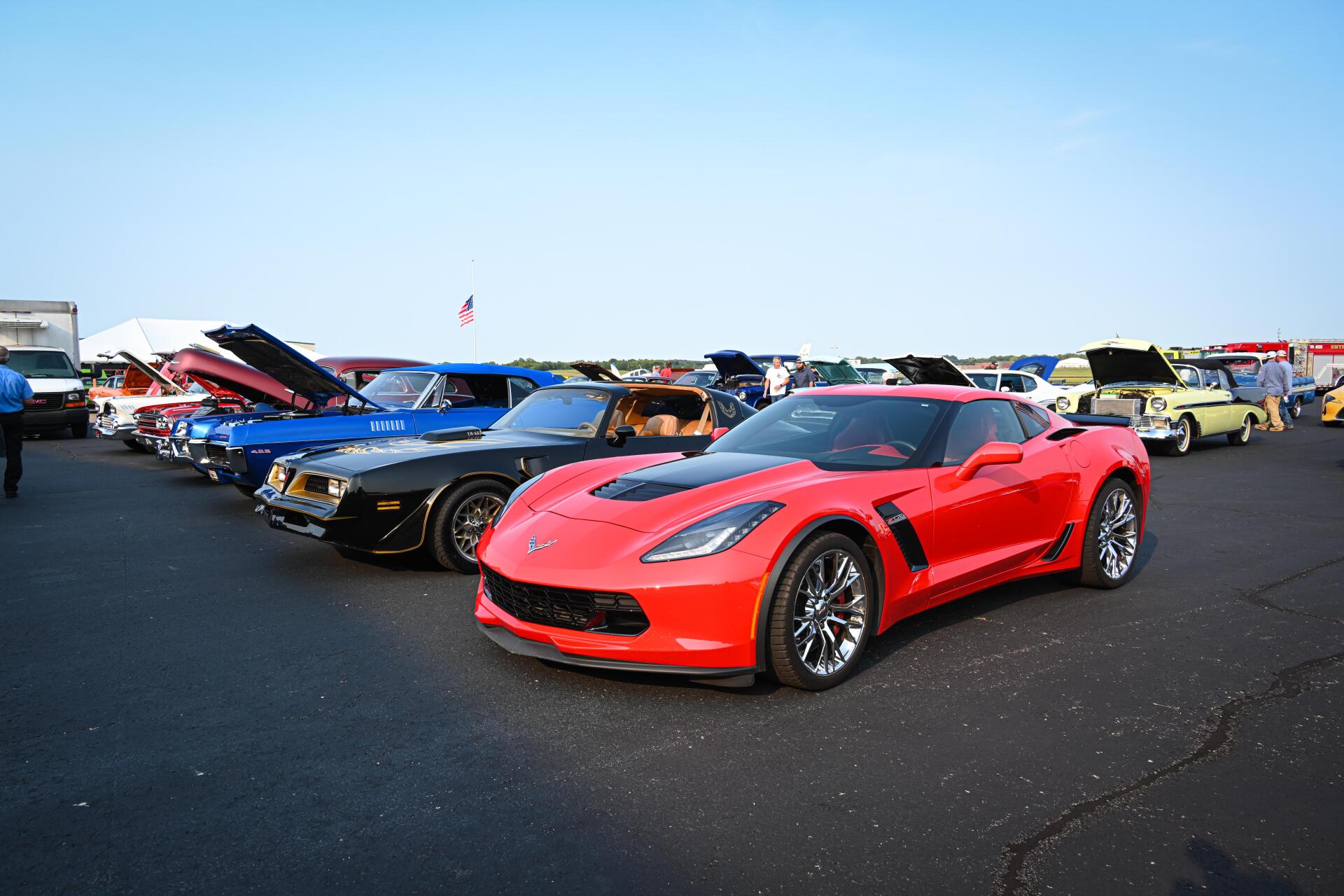 A red corvette is parked in a parking lot with other cars