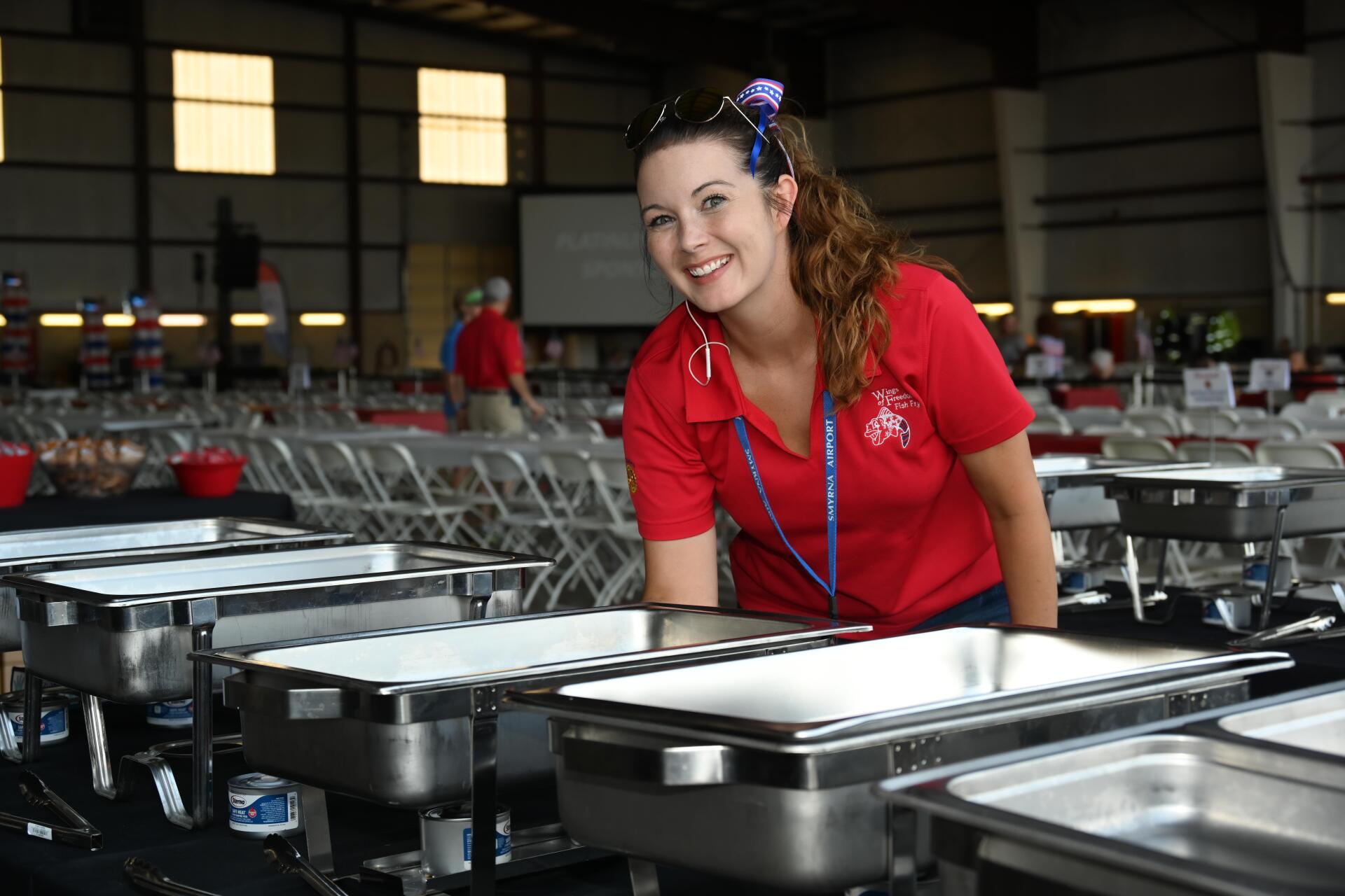 A woman in a red shirt is standing in front of a buffet line