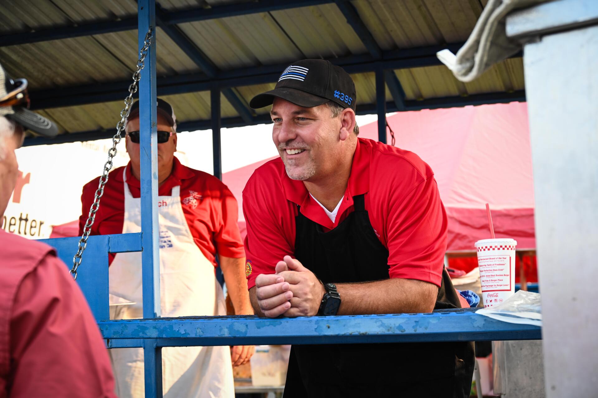 A man in a red shirt and black apron is smiling while sitting at a counter.