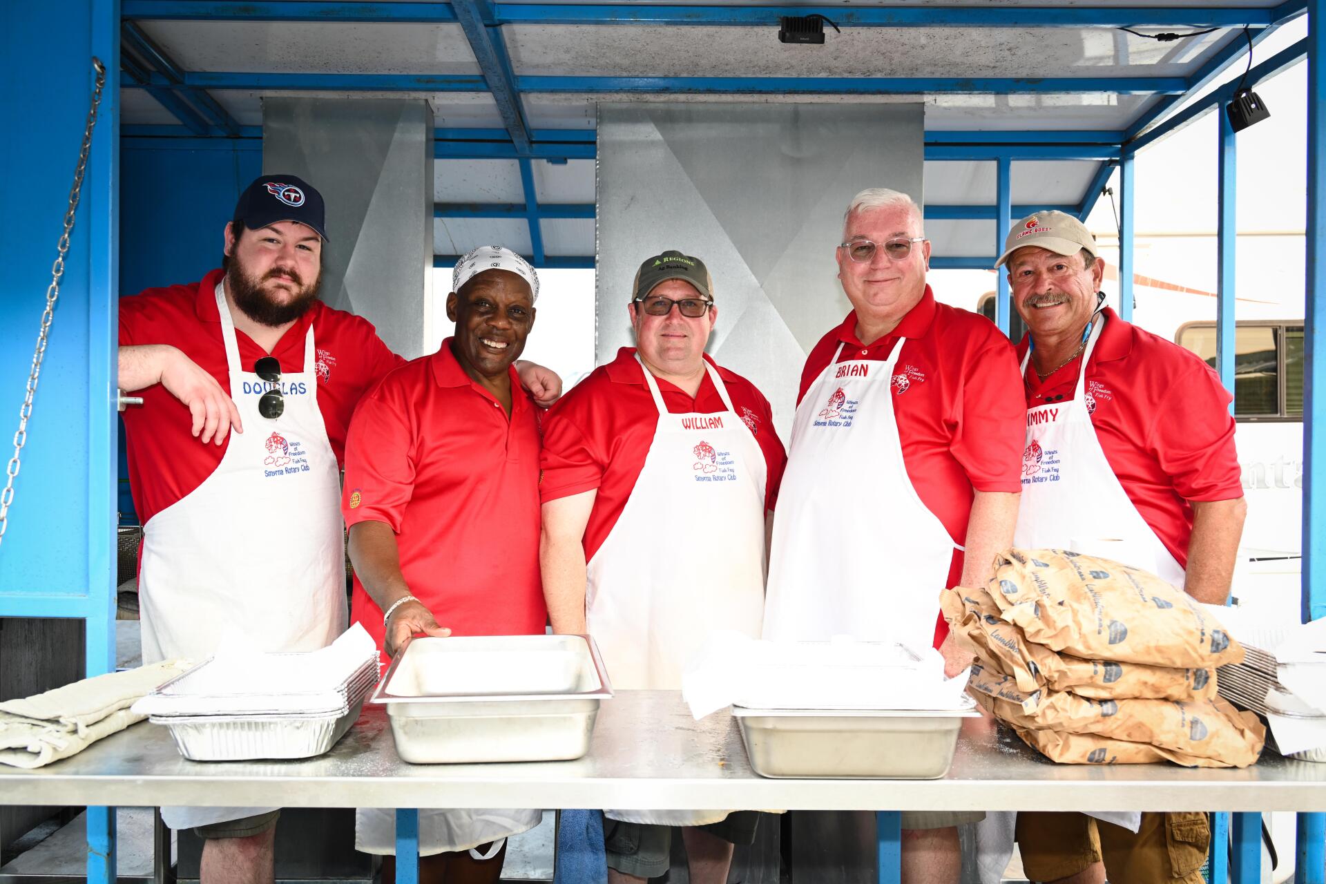 A group of men wearing aprons are standing in front of a table.