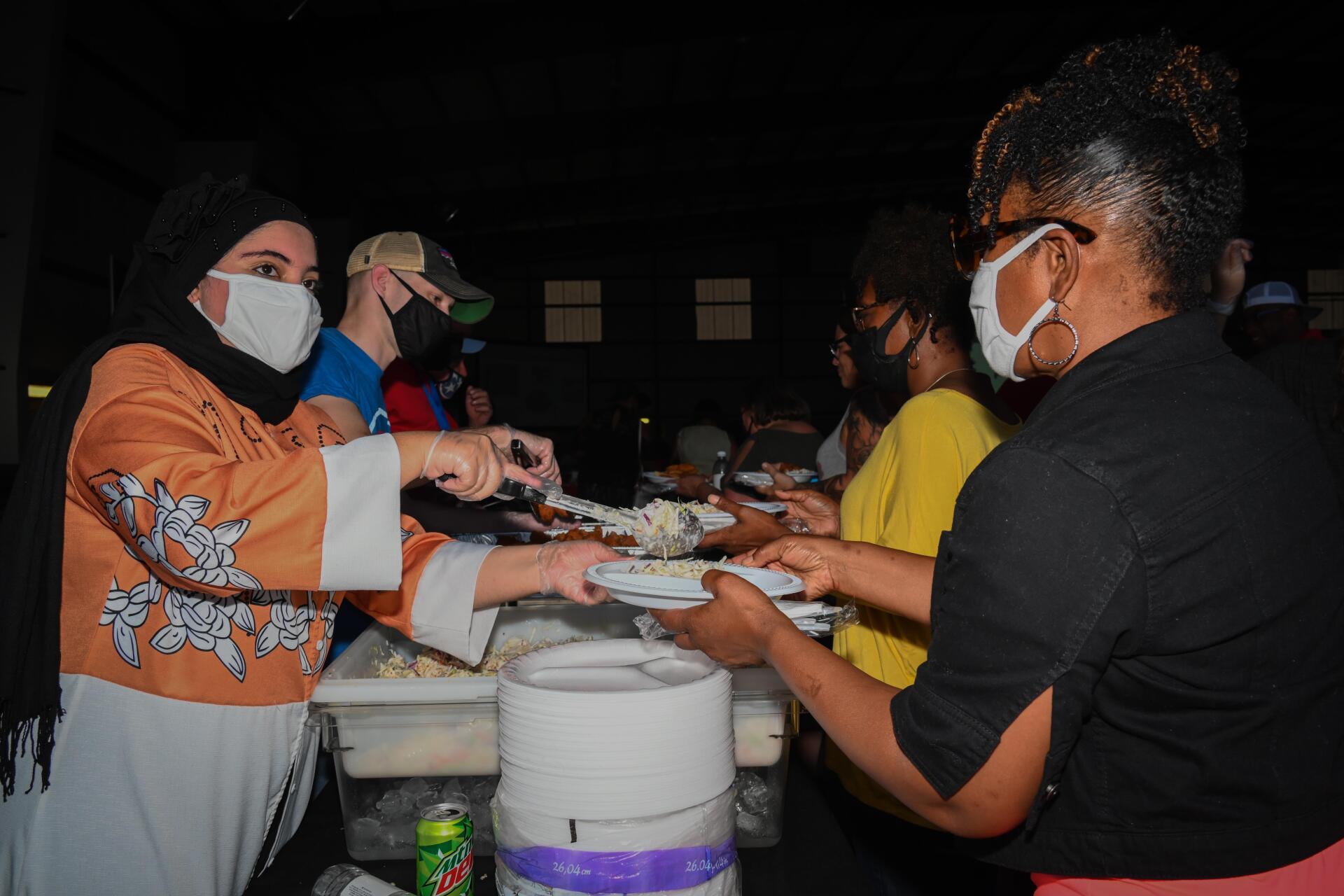 A woman wearing a mask is serving food to a group of people.