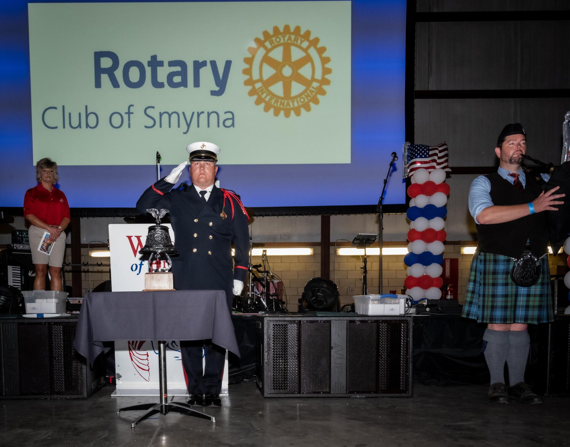 A man in a kilt stands in front of a sign that says rotary club of smyrna