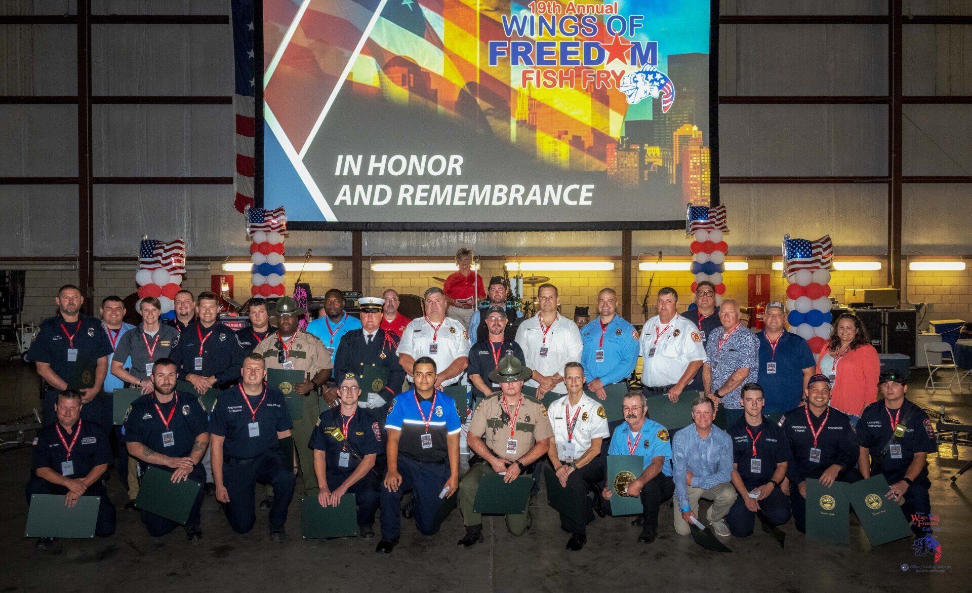 A group of people are posing for a picture in front of a large screen that says in honor and remembrance.