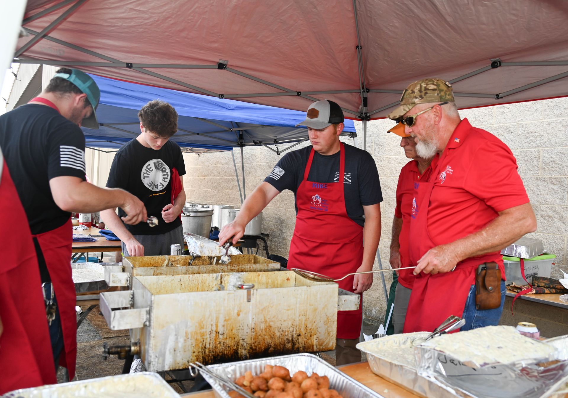 A group of men in red aprons are preparing food under a tent.
