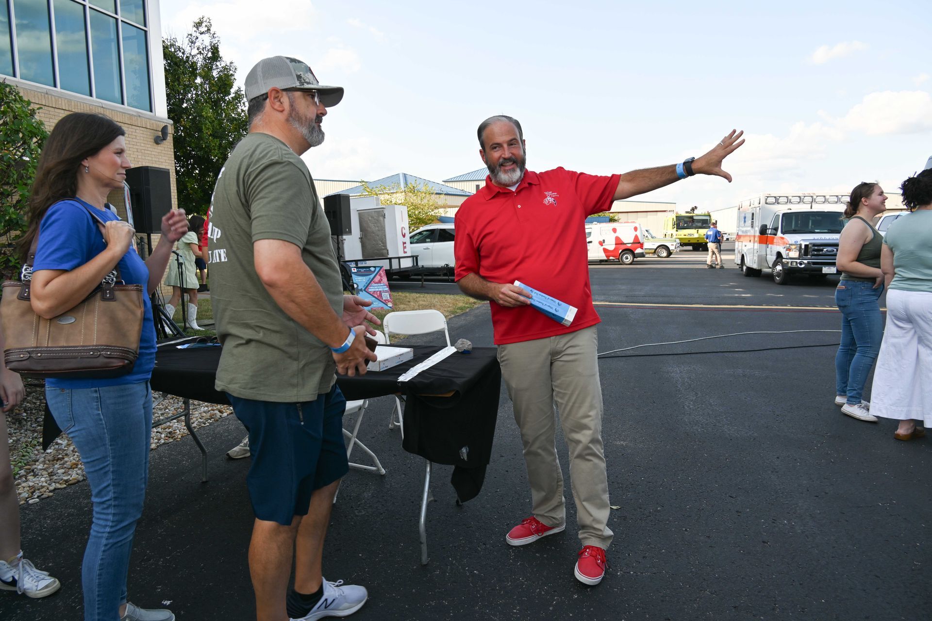 A man in a red shirt is talking to a group of people in a parking lot.