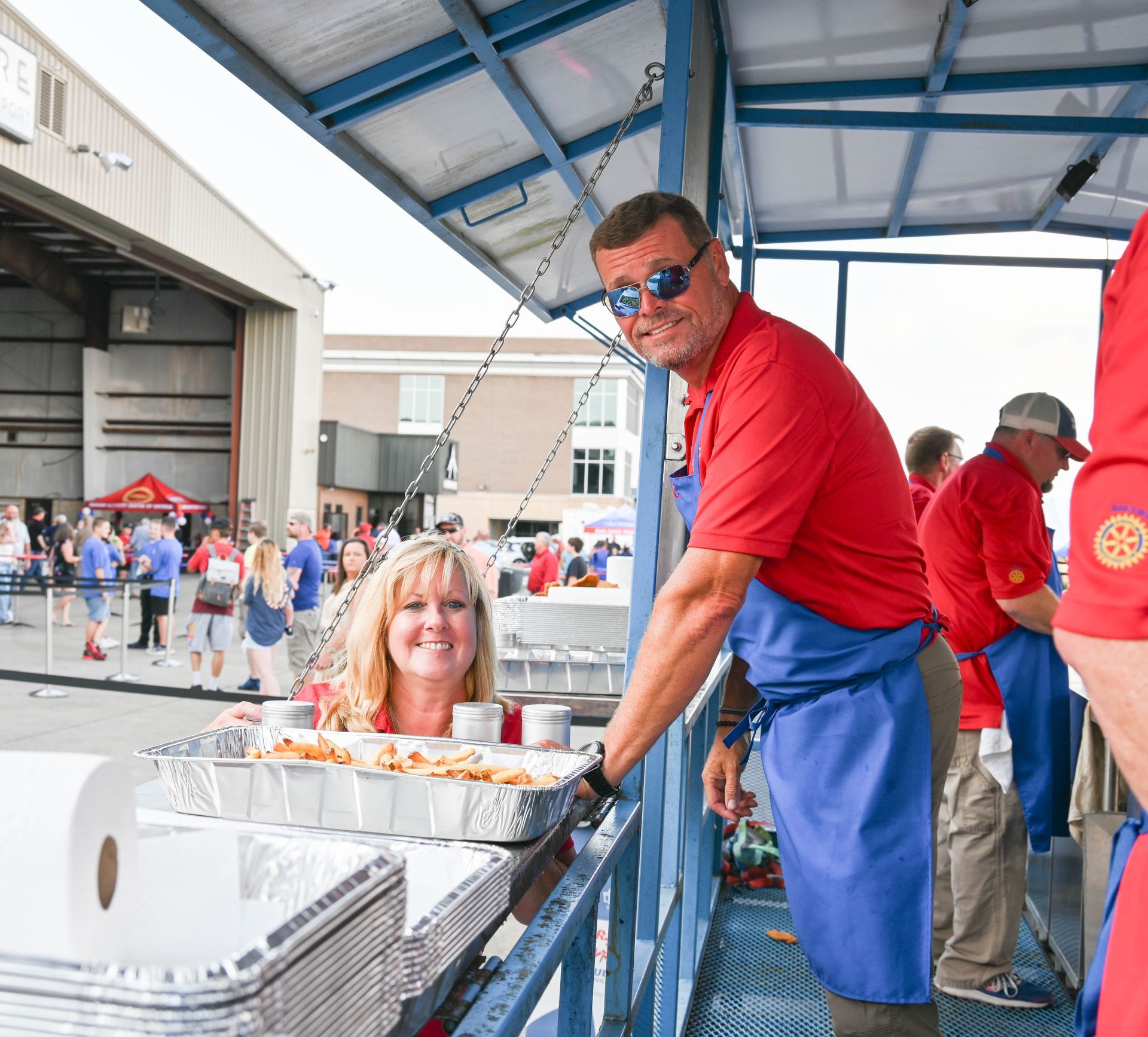 A man in a red shirt is standing next to a woman in a blue apron