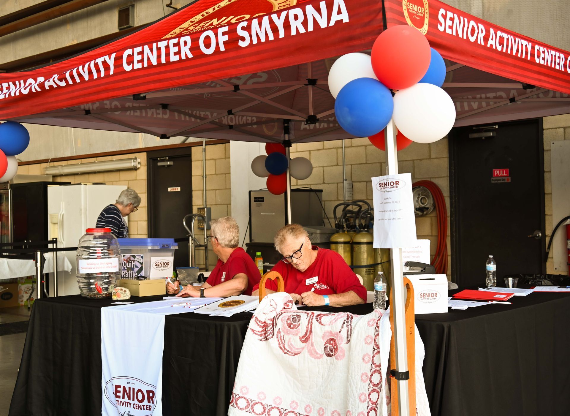 Two men are sitting at a table under a tent that says senior activity center of smyrna