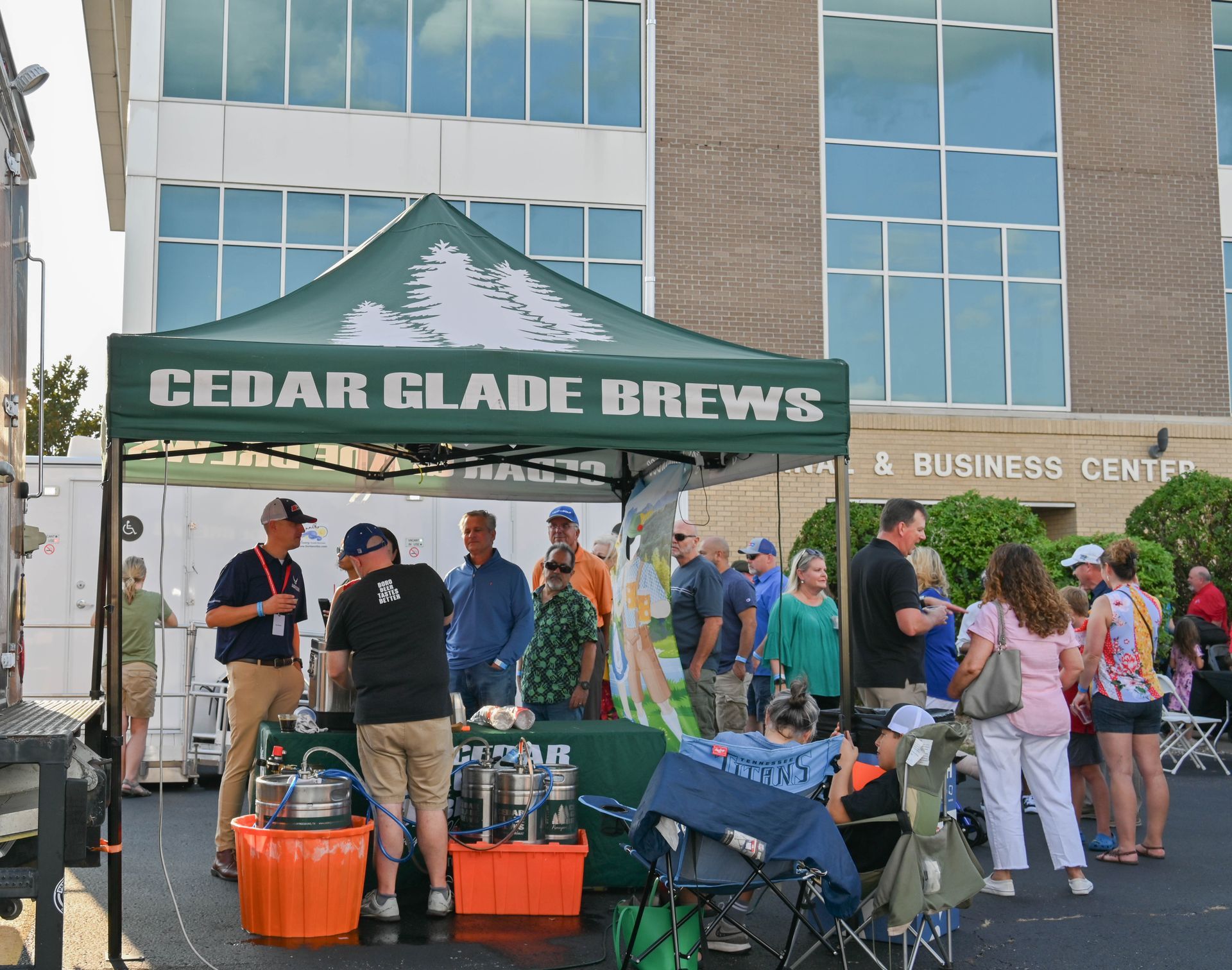 A group of people are gathered under a tent that says cedar glade brews