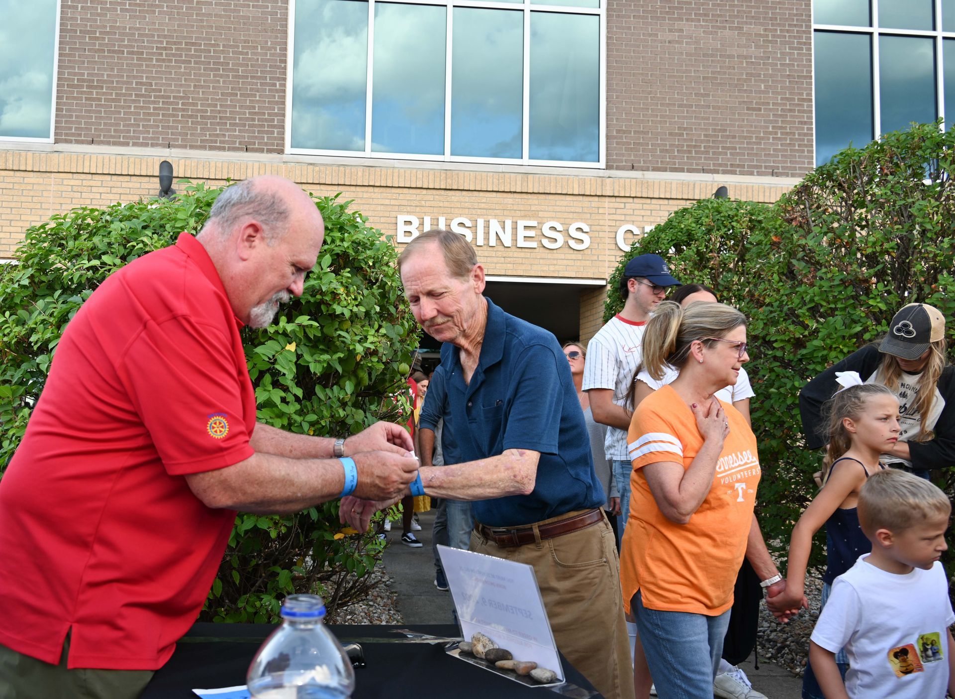 A man in a red shirt is giving a certificate to another man in front of a business center.