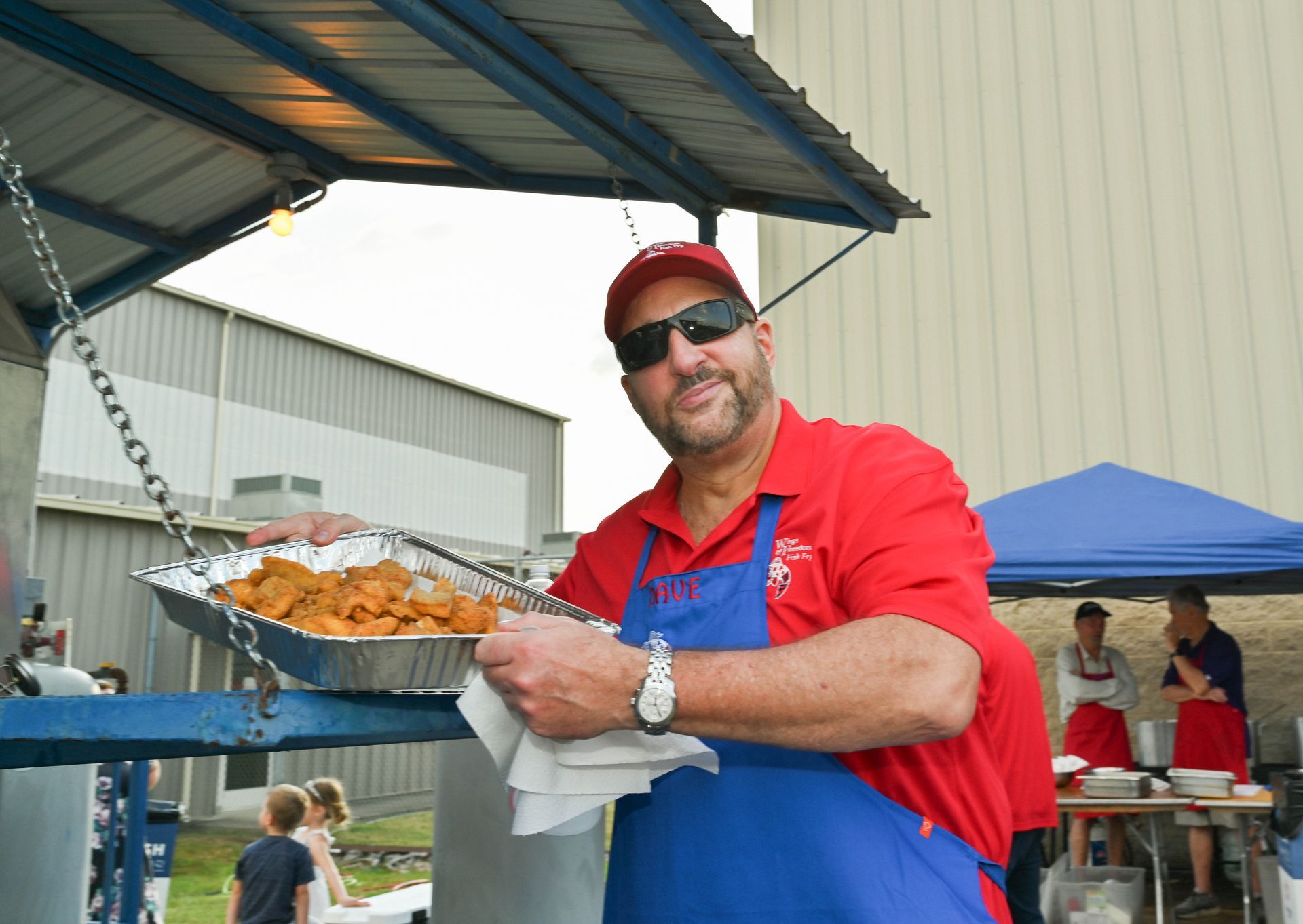 A man in a red shirt and blue apron is holding a tray of food.