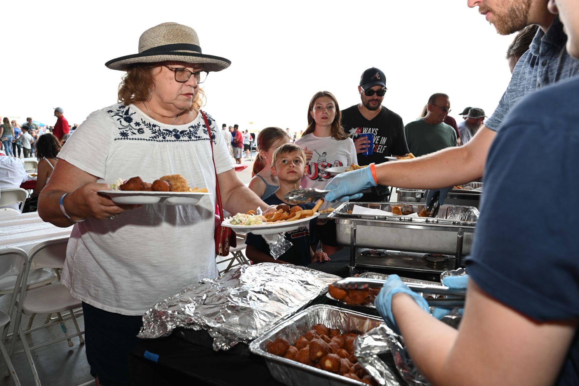 A woman in a hat is getting food from a buffet line.
