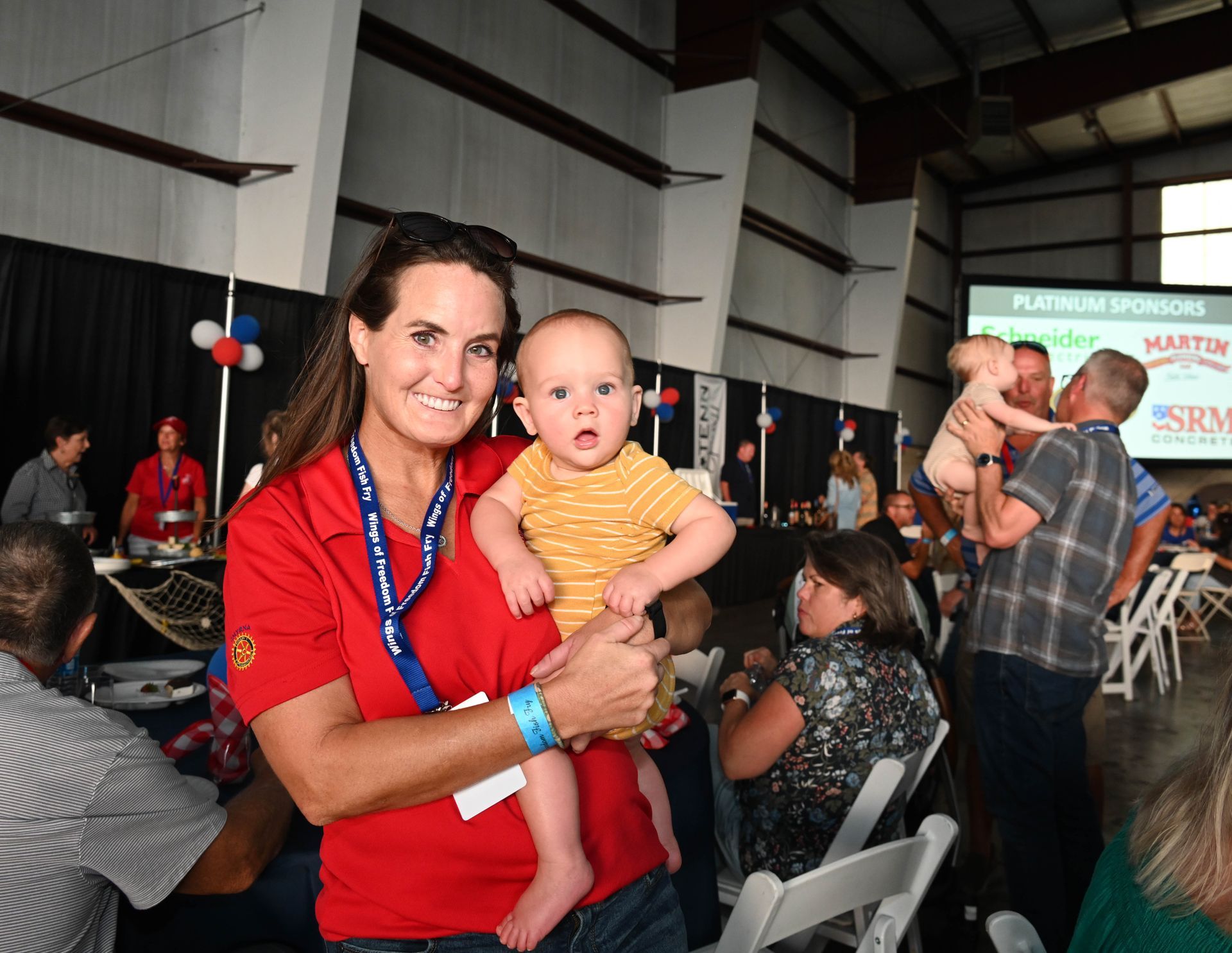 A woman in a red shirt is holding a baby in her arms.
