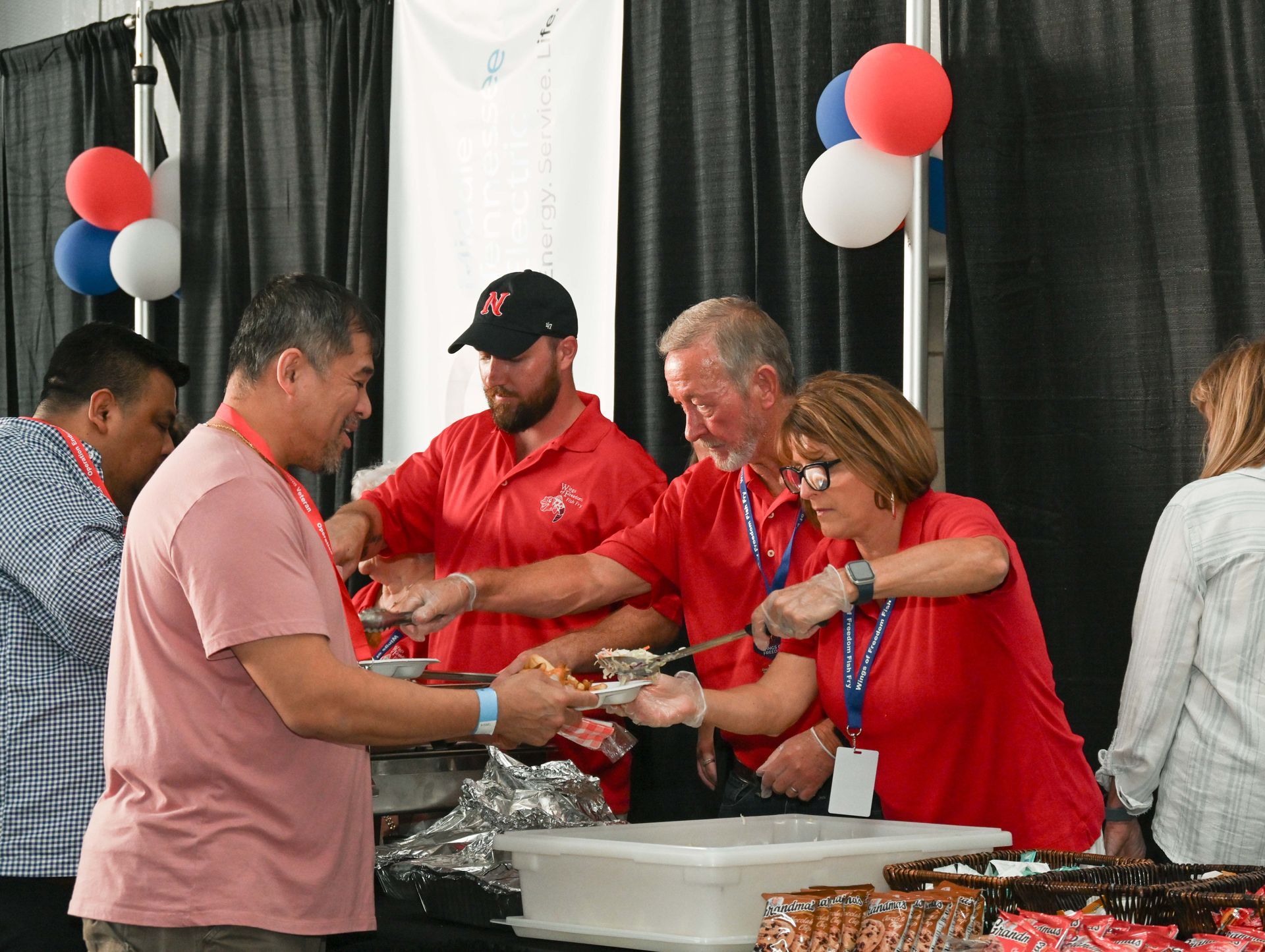 A group of people in red shirts are serving food to each other.