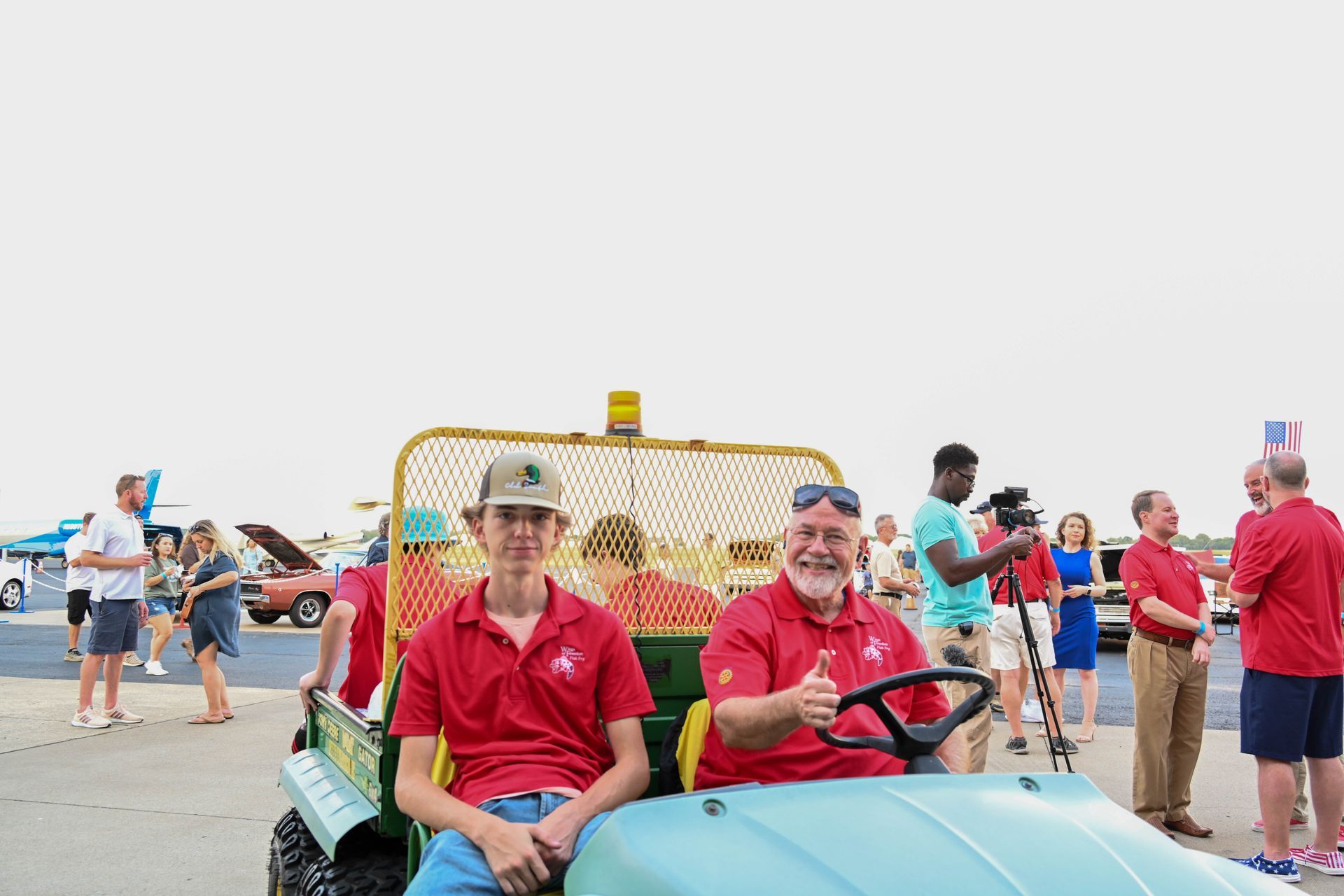 Two men are sitting in a golf cart and giving a thumbs up.