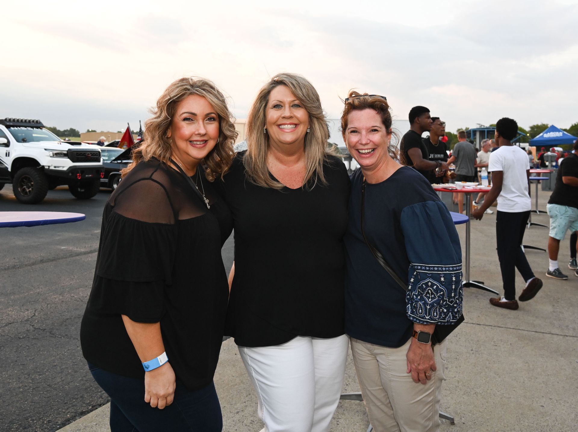 Three women are posing for a picture together in a parking lot.
