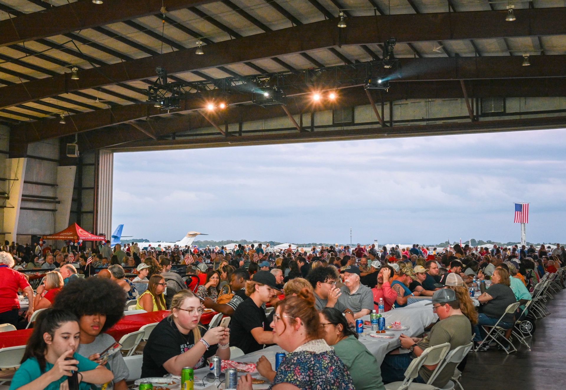 A large group of people are sitting at tables in an airplane hangar.