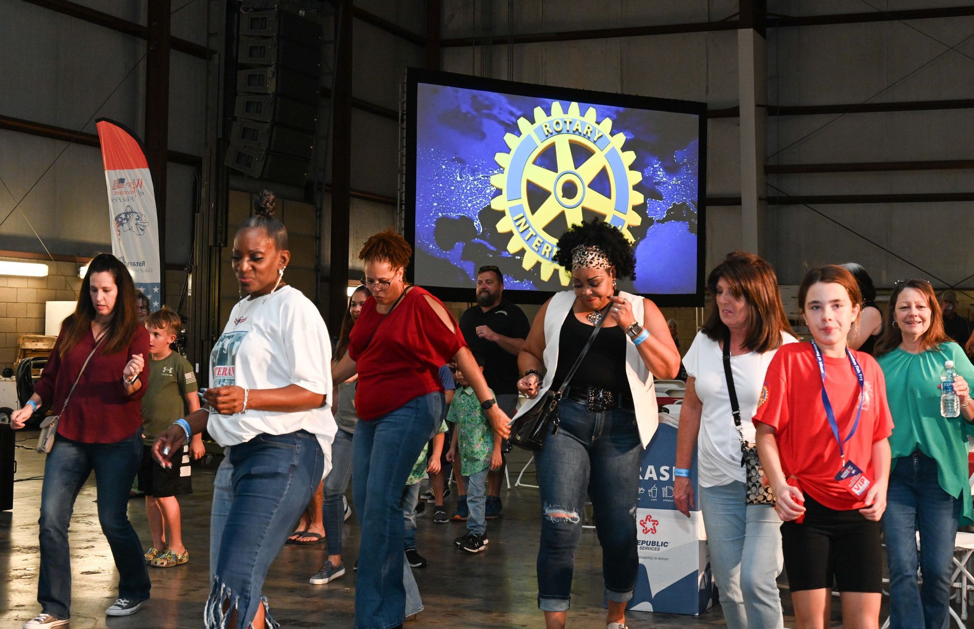 A group of people are dancing in front of a large screen.