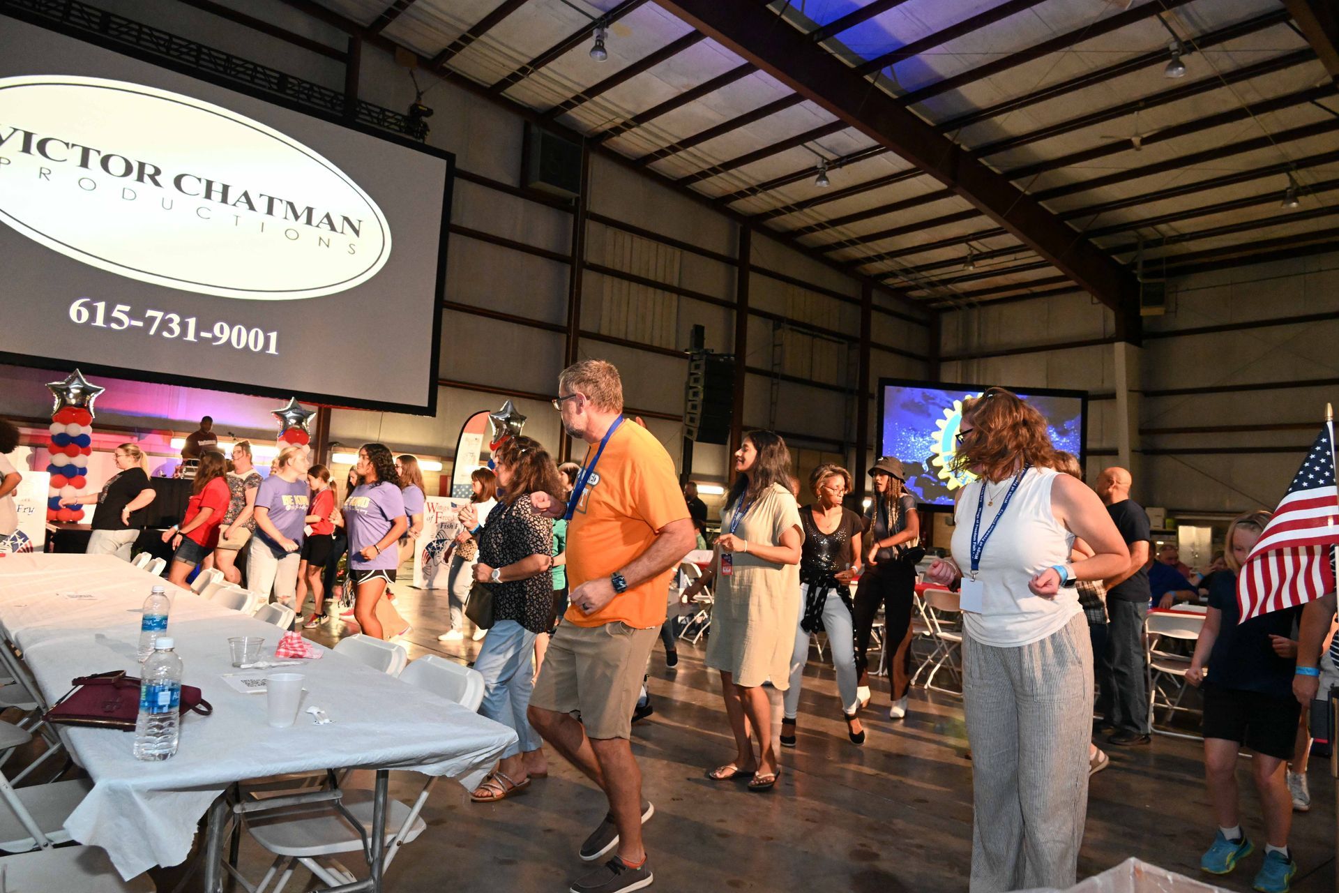 A group of people are dancing in a room with tables and chairs.