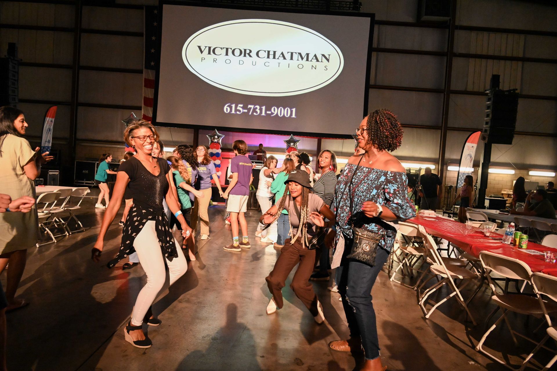 A group of people are dancing in front of a victor chatman sign.