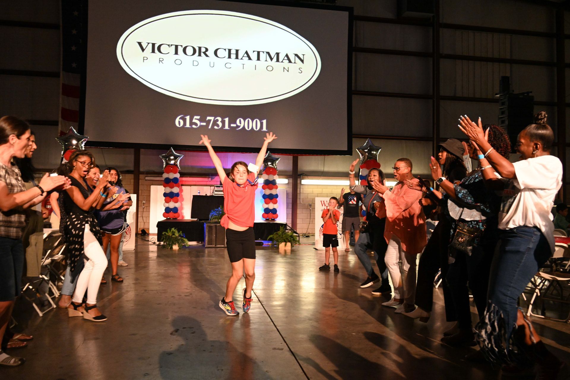 A group of people are dancing in front of a victor chatman sign.
