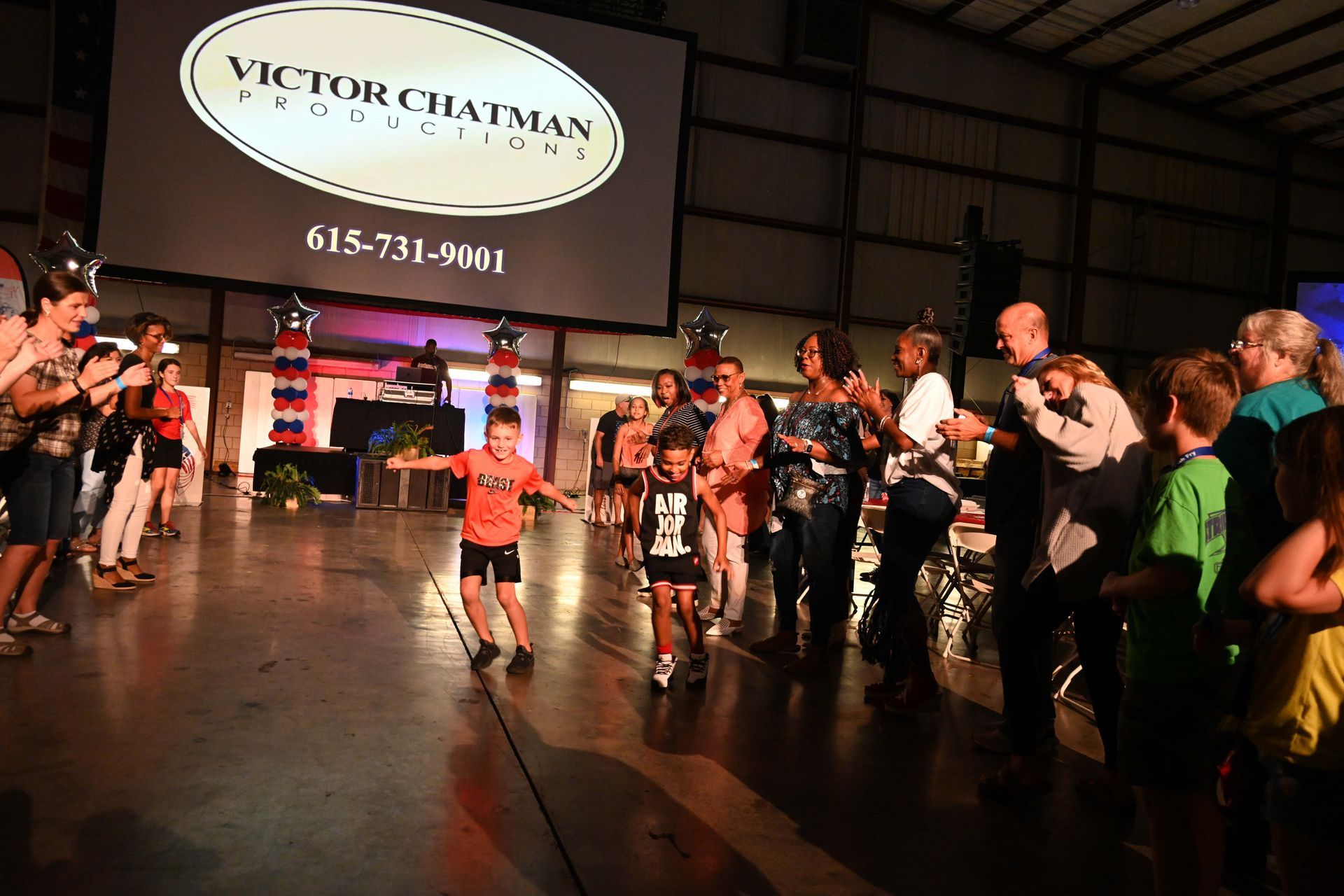 A group of people are dancing in front of a large screen that says victor chatman productions