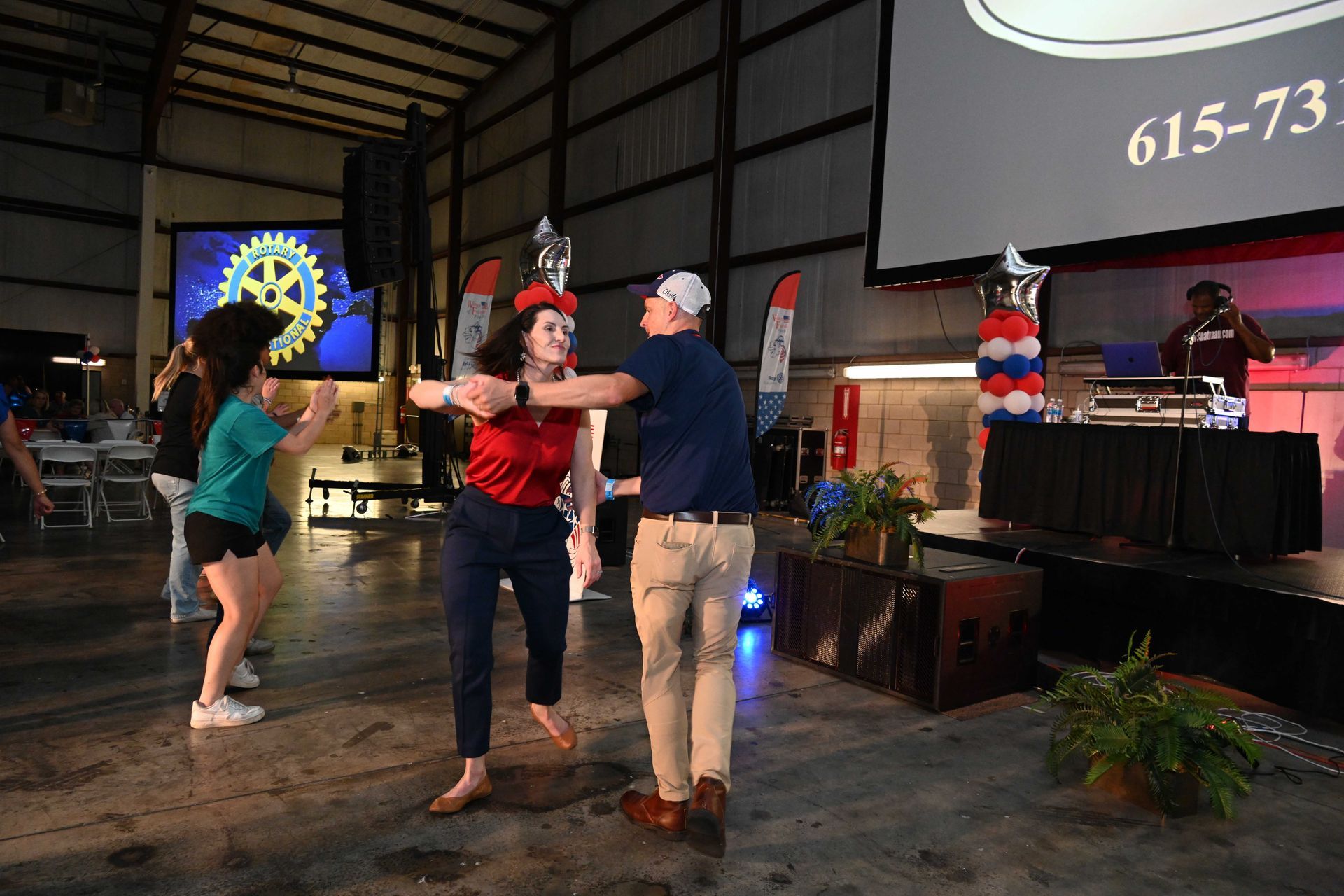 A group of people are dancing on a stage in front of a large screen.