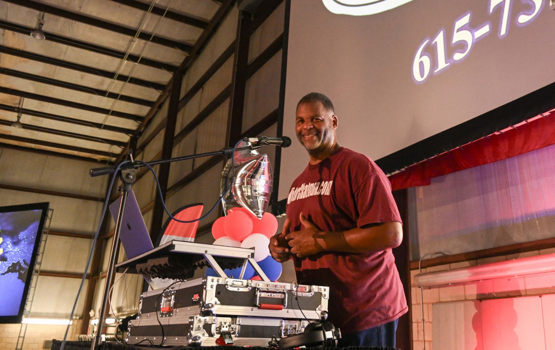 A man in a red shirt is standing in front of a screen that says 615-75