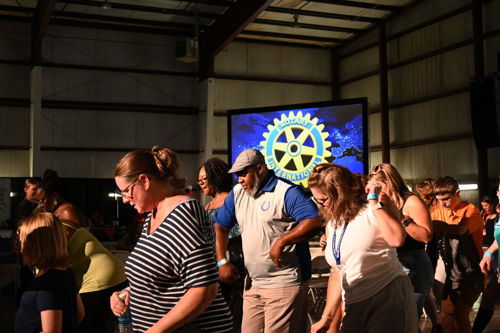A group of people are dancing in front of a large screen with a rotary logo on it.