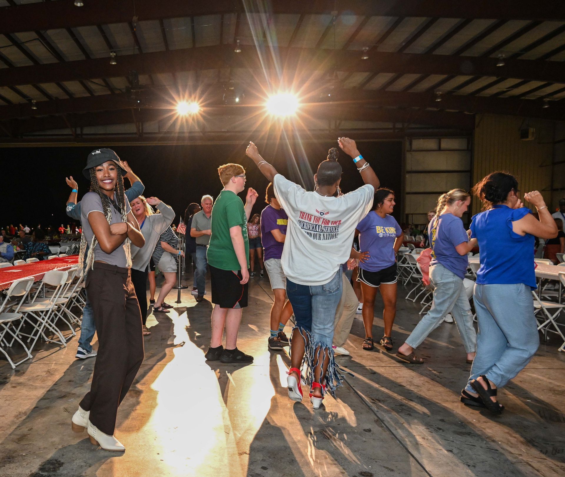 A group of people are dancing in a room with tables and chairs