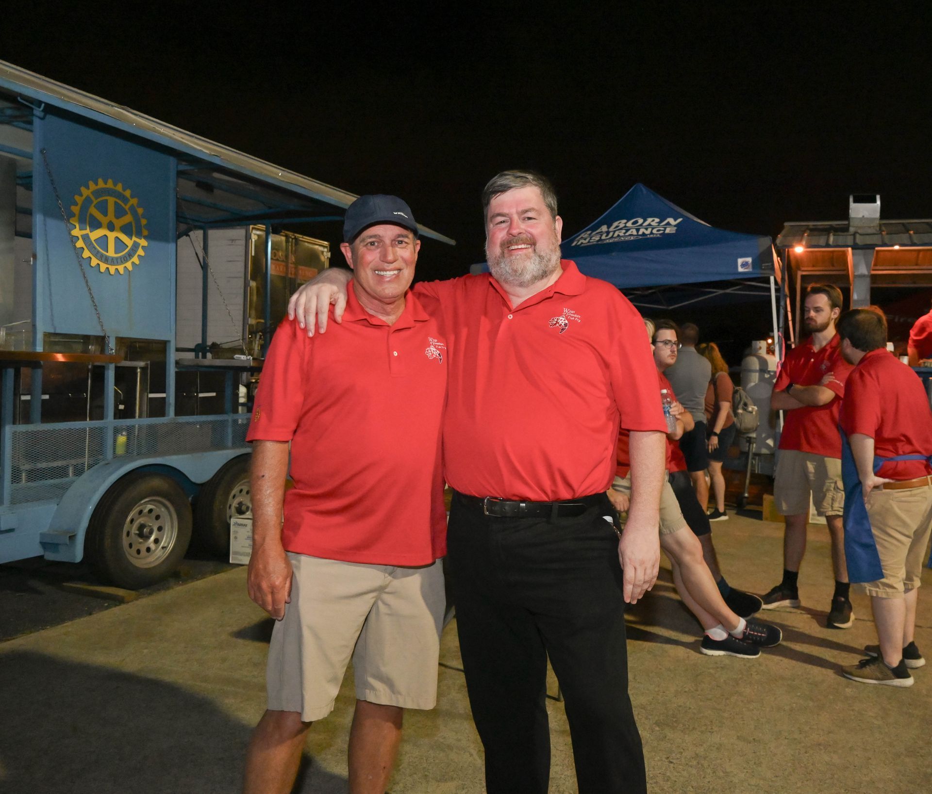 Two men are posing for a picture in front of a food truck that says rotary